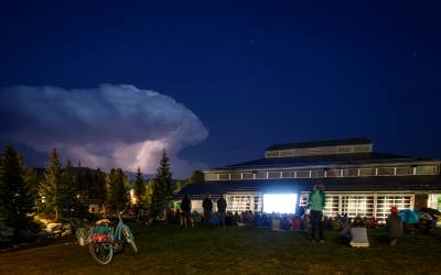 The exterior of the Riverwalk Center in Breckenridge at night with a thunderstorm on the horizon