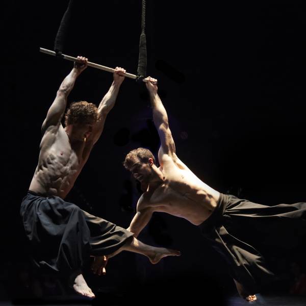 Circa contemporary circus company - be drawn into the deep world of physical daring with a hauntingly beautiful exploration of what is possible with the human body. Shown here are two male trapeze artists performing.