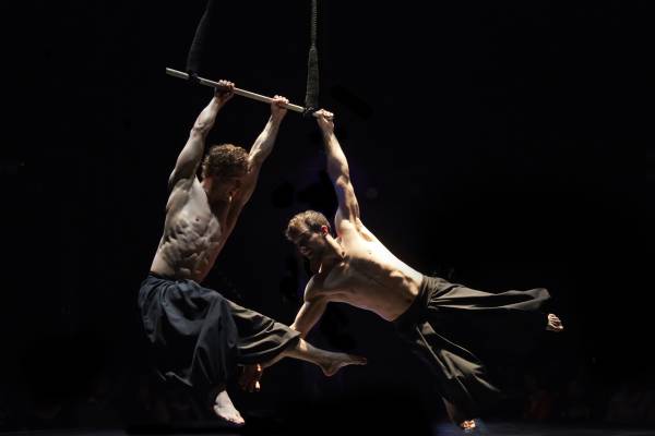 Circa contemporary circus company - be drawn into the deep world of physical daring with a hauntingly beautiful exploration of what is possible with the human body. Shown here are two male trapeze artists performing.