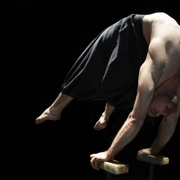 Circa contemporary circus company. Shown here a male acrobat balancing himself on two small wooden beams while in a scorpion style handstand